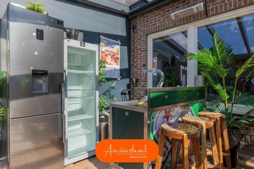 an outdoor kitchen with a refrigerator and stools at Amsterdam Group Stay - 26 Beds - Jacuzzi & Sauna in Zwanenburg