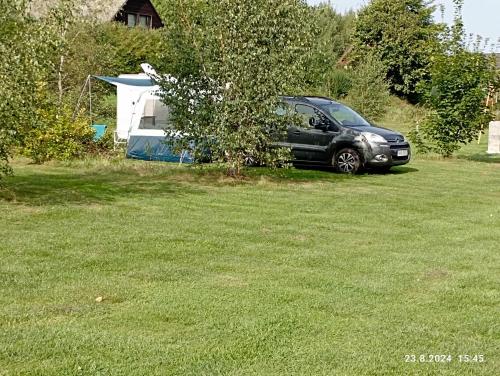 a black car parked in a yard next to a tent at Stellplatz Božanov in Božanov