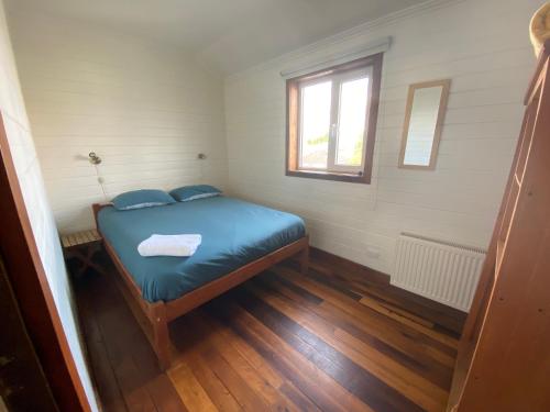 a small room with a bed with blue sheets and a window at Hostal Compass del Sur in Puerto Varas