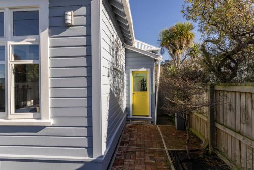 a yellow door on a house with a fence at Once upon a Cosy Nook in Dunedin