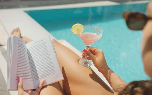 a woman laying in a pool reading a book and a drink at Santa Lucia Boutique Hotel in Santa Luċija