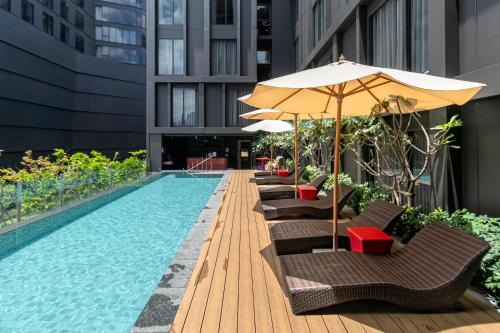 a pool with chairs and an umbrella next to a building at Oakwood Studios Sukhumvit Bangkok in Bangkok