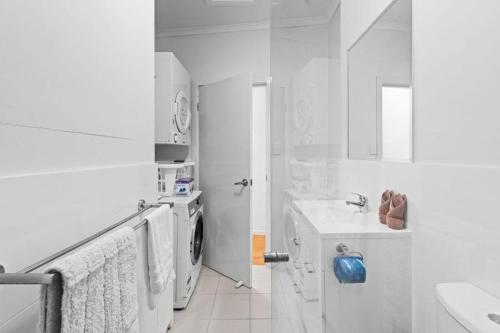 a white bathroom with a washing machine and a sink at modern apartment in the heart of Norman Park in Brisbane