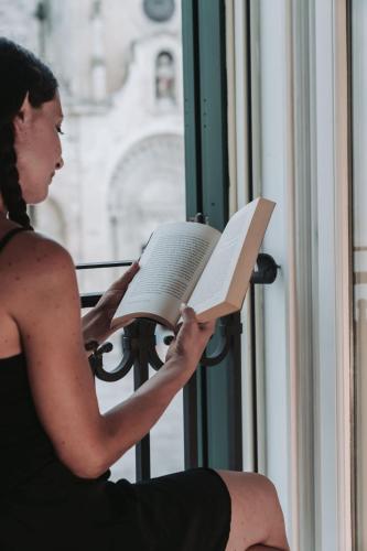 a woman sitting on a window sill reading a book at La Casa di Ele in Matera
