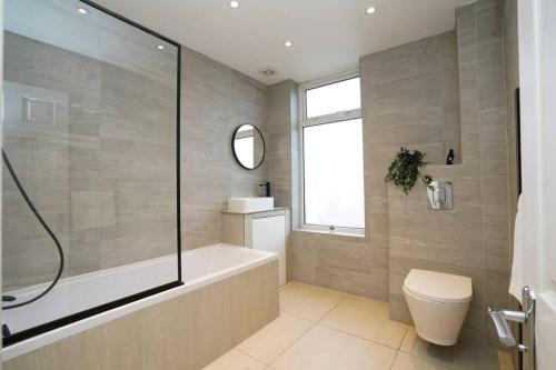 a bathroom with a tub and a toilet and a window at 3 Bedroom Home with Free parking in Leeds