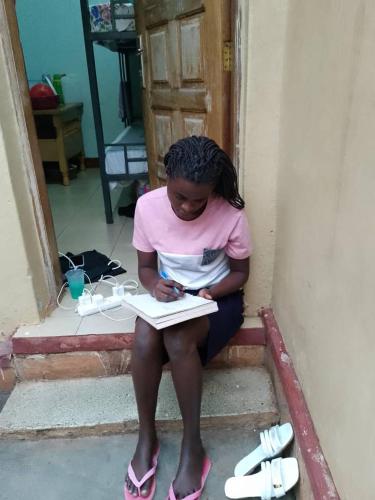 a girl sitting on the steps writing in a book at HGAD foundation in Jinja
