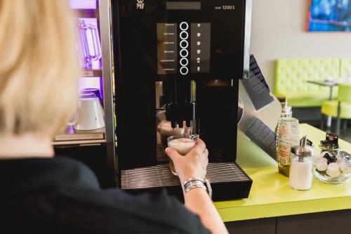 a woman is making a drink in a coffee machine at SleepySleepy Hotel Dillingen in Dillingen an der Donau