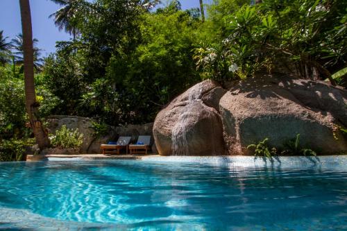 a swimming pool with two chairs and a large rock at Monkey Flower Villas in Koh Tao