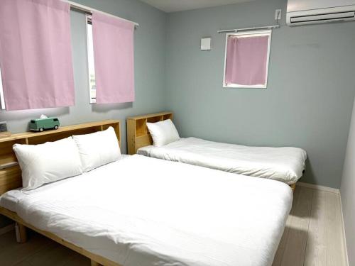 two beds in a room with white sheets and pink windows at M&Y Ishigaki Island / 3 Bedroom House in Ishigaki Island