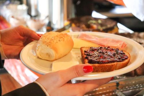a person holding a plate with a sandwich and a piece of bread at Pousada Campos do Jordao Suites in Campos do Jordão