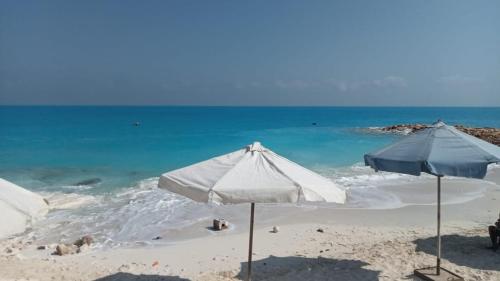 two white umbrellas on a beach with the ocean at 3 غرف و صاله جرين بيتش الساحل الشمالي للعائلات فقط in El Alamein