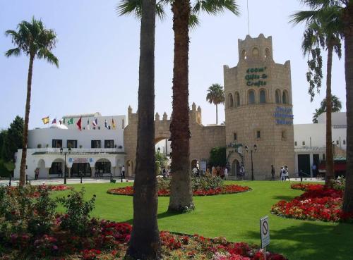 a building with a clock tower in a park with palm trees at Sousse Marina Kantaoui l'expérience côtière in Port El Kantaoui