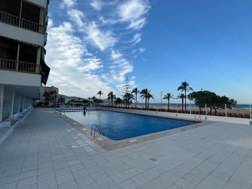 a swimming pool next to a building with palm trees at Apto. Cullera vistas espectaculares primera línea in Cullera