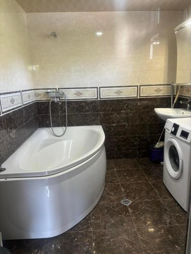 a bathroom with a tub and a sink and a washing machine at taisya guest house in Borjomi