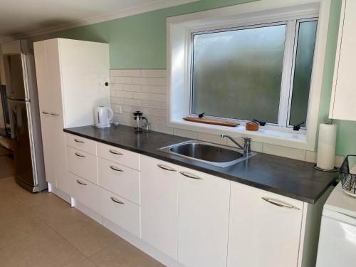 a kitchen with white cabinets and a sink and a window at Churchill Oasis by the sea in Tauranga