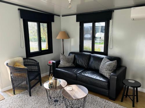 a living room with a black leather couch and two windows at Adorable little container house in Hastings