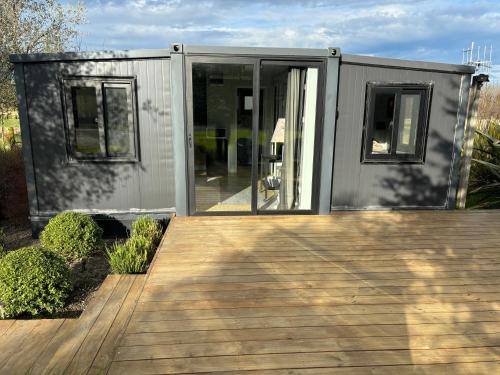 a small gray house with a wooden deck at Adorable little container house in Hastings