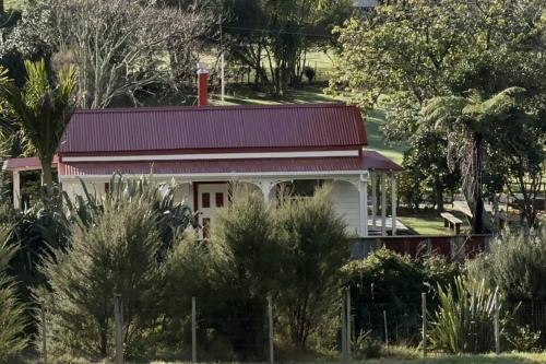 a white house with a red roof and trees at Heart Of Gold Cottage in Coromandel Town