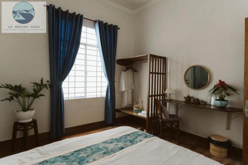 a bedroom with a bed and a window with blue curtains at Le Mékong Bleu in Ben Tre