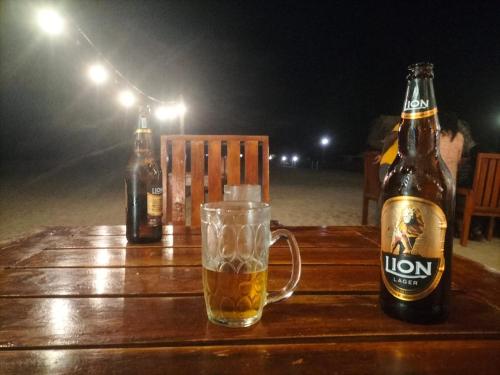 a bottle of beer and a glass on a wooden table at Hotel Coral Bay in Trincomalee