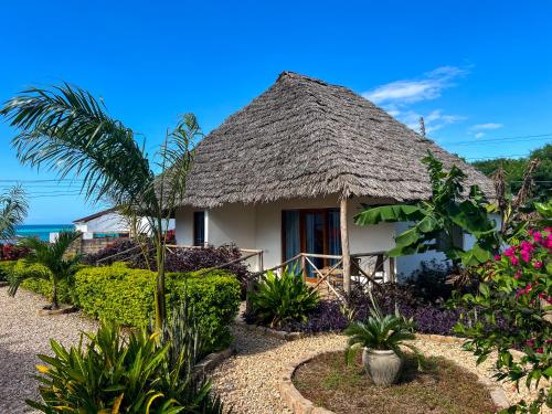 a house with a thatched roof in a garden at Kokopelli Bungalows in Nungwi