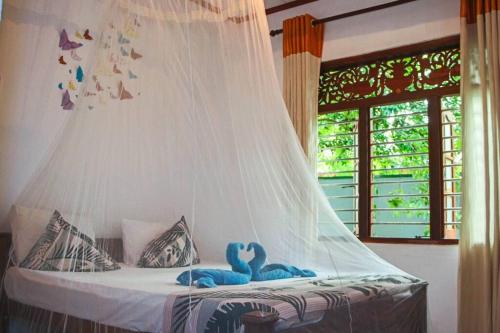 two blue swans sitting on a bed with a mosquito net at Lakmali Homestay in Watagederamulla