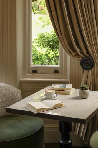 a table with books and a cup of coffee and a window at The Chelsea Townhouse by Iconic Luxury Hotels in London
