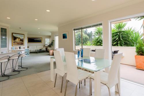 a dining room with a glass table and white chairs at Seascape Villa B&B in Tauranga