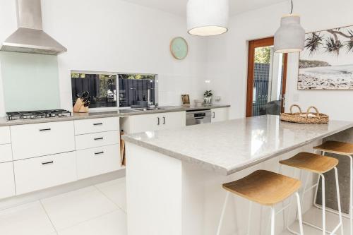 a white kitchen with a large counter and stools at Breezy Beach House - Private Pool in Yaroomba