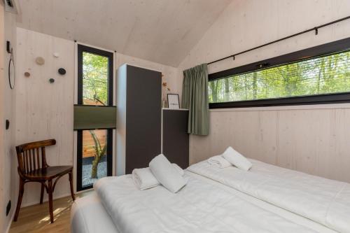 a bedroom with two beds and a chair and windows at Welcome in - Tinyhouse La Mouette met zonnig terras, Zoutelande in Zoutelande