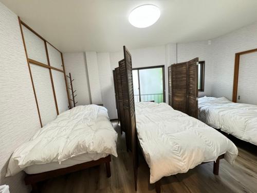 two beds in a room with white sheets at 宿坊かつら in Izu