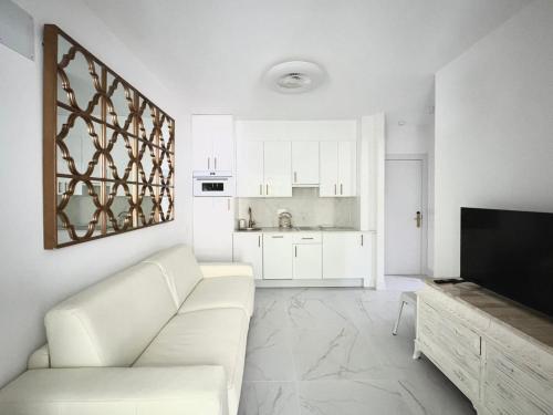 a white living room with a white couch and a television at El Jardín de María Luisa Suites in Burgos