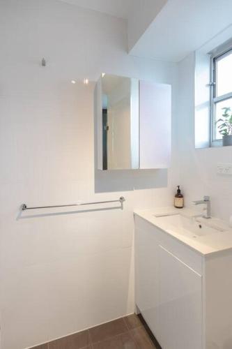 a white bathroom with a sink and a mirror at Cozy Studio walk to Park & Water in Sydney