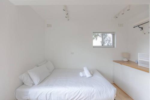 a white bed in a white room with a window at Cozy Studio walk to Park & Water in Sydney