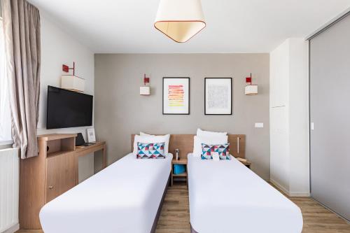 two beds in a room with a flat screen tv at Appart'City Confort Orléans in Orléans