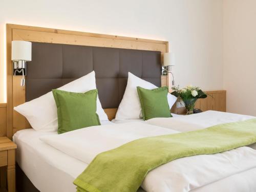 two white beds with green pillows in a bedroom at Vitalhotel Marienhof in Velden am Wörthersee