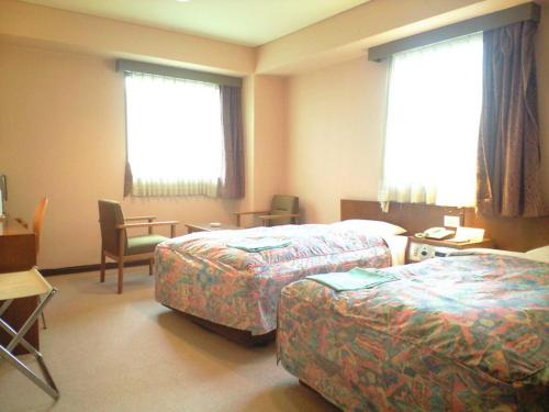高松市にあるホテル高松ヒルズのベッド2台とデスクが備わるホテルルームです。