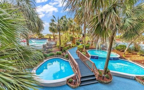 an image of two pools at a resort with palm trees at Modern Oceanfront 1 Bedroom Condo, Prime Location, Stunning Views at Beach Cove Resort in Myrtle Beach