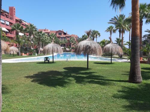 a swimming pool with straw umbrellas in a park at Costa Tropical Comfortable Apartment Playa Granada in Motril
