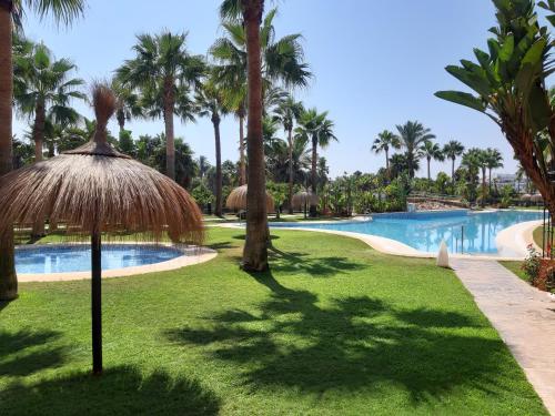 a resort pool with a straw umbrella and palm trees at Costa Tropical Comfortable Apartment Playa Granada in Motril