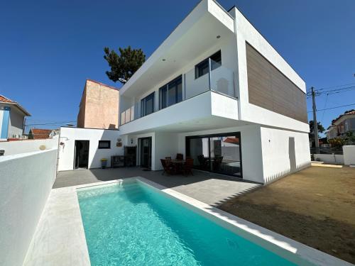 a white house with a swimming pool in front of it at Maison bord mer près de le Lisbonne in Charneca