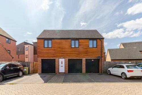 a wooden house with two garage doors and two cars at Lovely Apartment with Garden & Parking in Milton Keynes