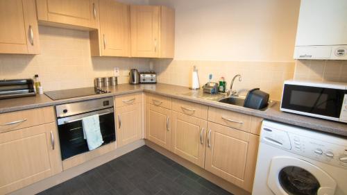 cocina con armarios de madera, lavadora y secadora en Morris Gardens Apartments en Oldmeldrum