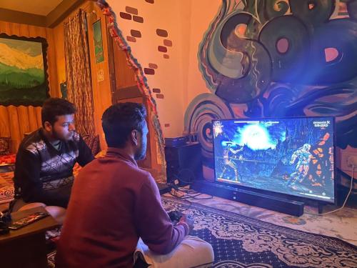 two men playing a video game on a television at Eye love peace cafe in Manīkaran