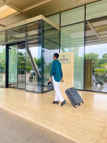 a woman walking with a suitcase in front of a building at Radisson Collection Hotel Bamako in Bamako