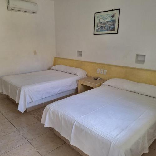 two beds in a room with white sheets at Hotel Anturios in Zihuatanejo