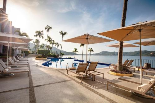a pool at a resort with chairs and umbrellas at Camino Real Acapulco Diamante in Acapulco
