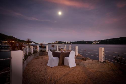a table with white chairs sitting on the beach at night at Camino Real Acapulco Diamante in Acapulco