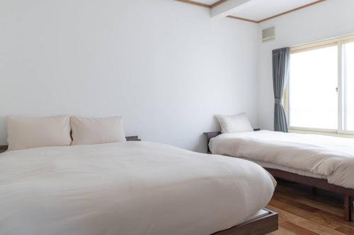 a white bedroom with two beds and a window at KAKUREGA by unito in Hakodate