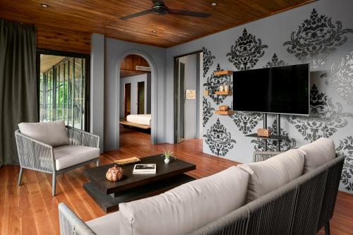 a living room with a couch and a tv on a wall at The Namkhan, a Small Luxury Hotel of the World in Luang Prabang